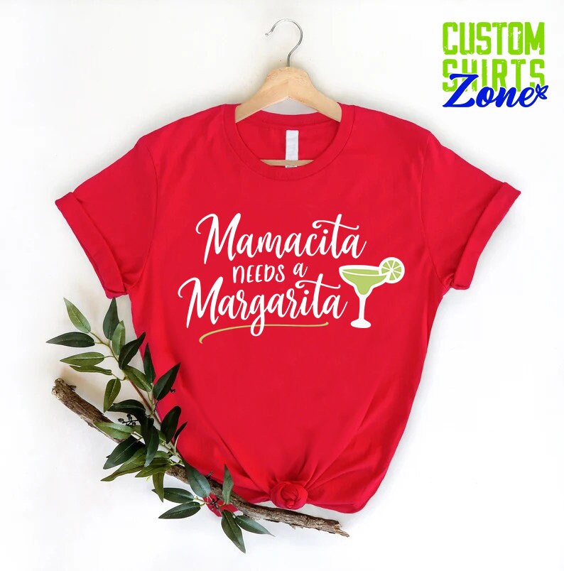 May include: Red t-shirt with white text that reads "Mamacita needs a Margarita" and a green margarita glass with a lime wedge.