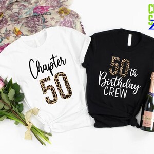 May include: Two t-shirts, one white and one black, with a leopard print design. The white shirt says "Chapter 50" and the black shirt says "50th Birthday Crew".