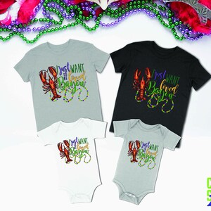 May include: Four shirts with a crawfish and beads design. The shirts say "I just want to be loved in Bayou". The shirts are in different sizes and colors.