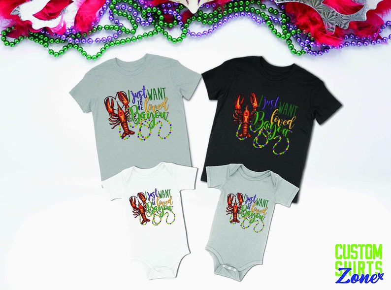 May include: Four shirts with a crawfish and beads design. The shirts say "I just want to be loved in Bayou". The shirts are in different sizes and colors.