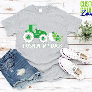 May include: A gray t-shirt with a green tractor and shamrocks, and the text "Pushin' My Luck".
