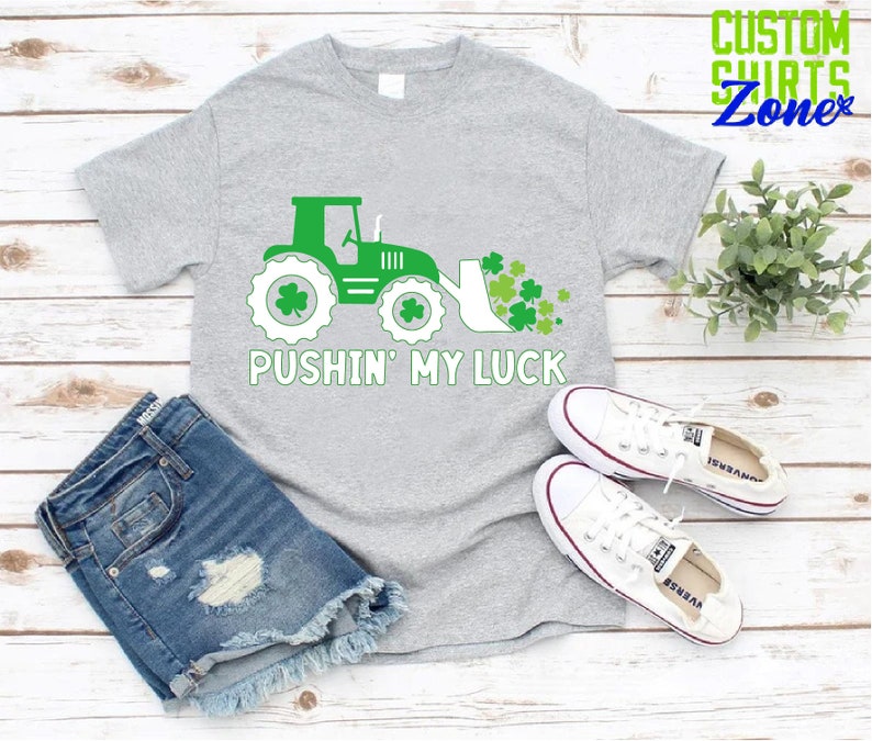 May include: A gray t-shirt with a green tractor and shamrocks, and the text "Pushin' My Luck".