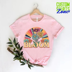May include: Pink t-shirt with a retro-style graphic of flowers and a rainbow with the word "BLOOM" in a vintage font.