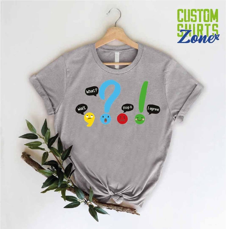 May include: Gray t-shirt with a graphic of punctuation marks with faces and speech bubbles. The text on the shirt reads "Wait", "What?", "Stop it", and "I agree!"