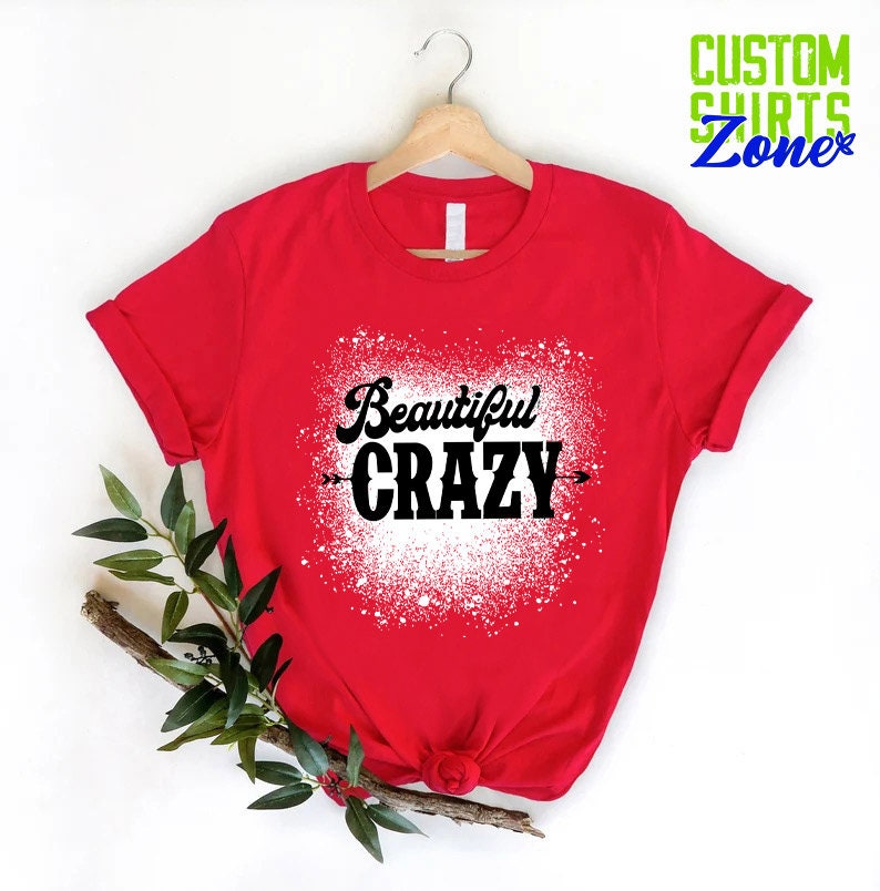 Puede incluir: Camiseta roja con un dise&ntilde;o de salpicaduras blancas y el texto "Beautiful CRAZY" en negro.