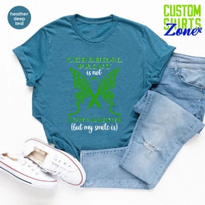 May include: A teal blue t-shirt with a green butterfly design and the text "Cerebral Palsy is not contagious (but my smile is)".
