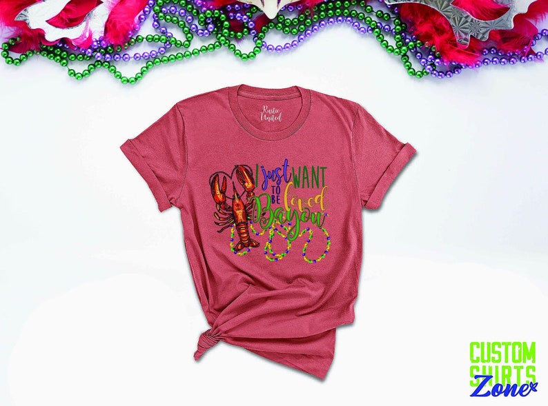 May include: A red t-shirt with a graphic of a crawfish and the text "I just want to be loved in the Bayou".