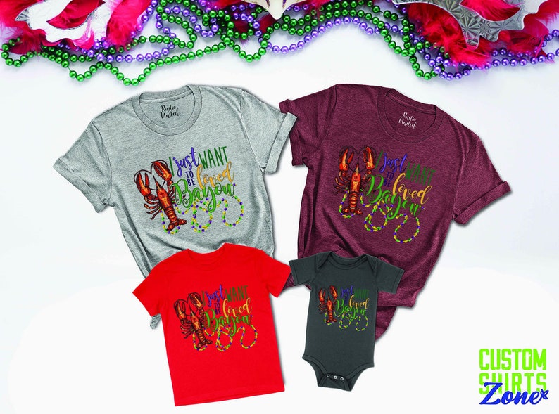 May include: A set of four shirts featuring a crawfish design with the text "I just want to be loved in da bayou". The shirts are in grey, maroon, red, and dark grey.