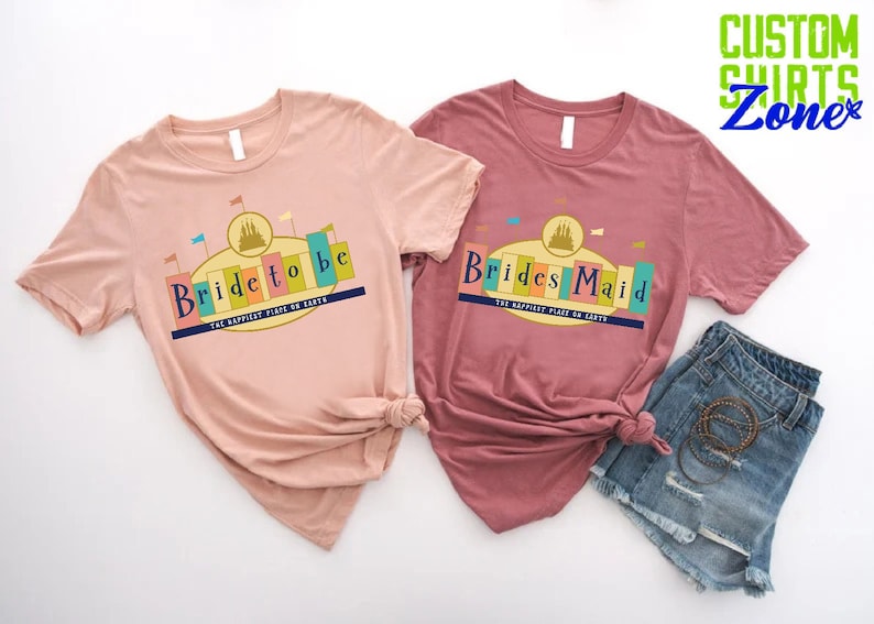 Puede incluir: Dos camisetas de color rosa y granate con un gr&aacute;fico de un castillo y el texto "Bride to be" y "Brides Maid" con las palabras "The Happiest Place on Earth" debajo.