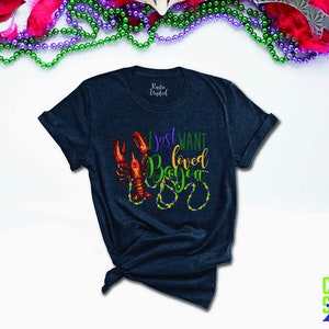 May include: A dark blue t-shirt with a graphic of a crawfish and beads that says "I just want loved Bayou".
