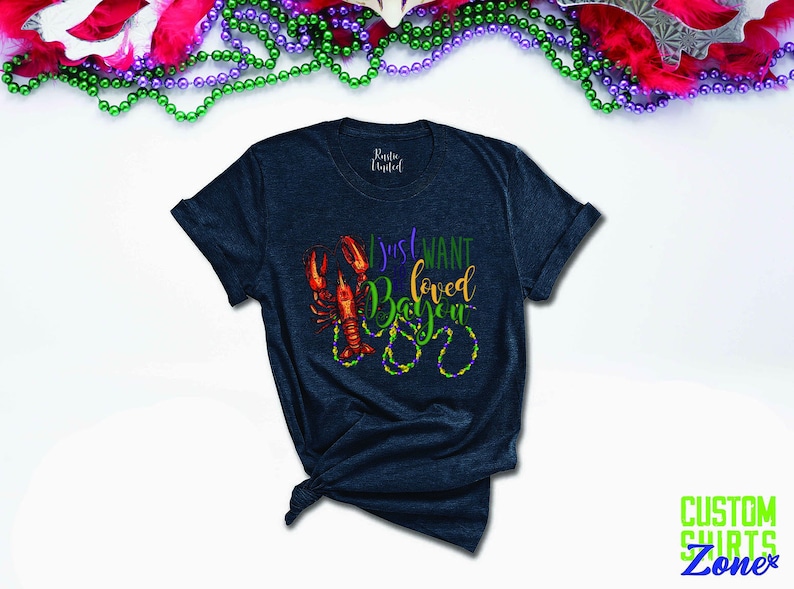 May include: A dark blue t-shirt with a graphic of a crawfish and beads that says "I just want loved Bayou".