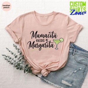 May include: A pink t-shirt with the text "Mamacita needs a Margarita" and a green margarita glass with a lime wedge.