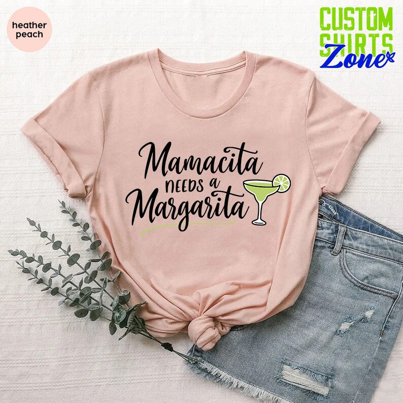 May include: A pink t-shirt with the text "Mamacita needs a Margarita" and a green margarita glass with a lime wedge.