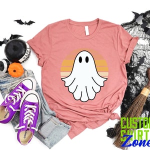 May include: A pink t-shirt with a white ghost silhouette in front of a retro sunset design. The text "CUSTOM SHIRTS ZONE" is visible in the bottom right corner of the image.