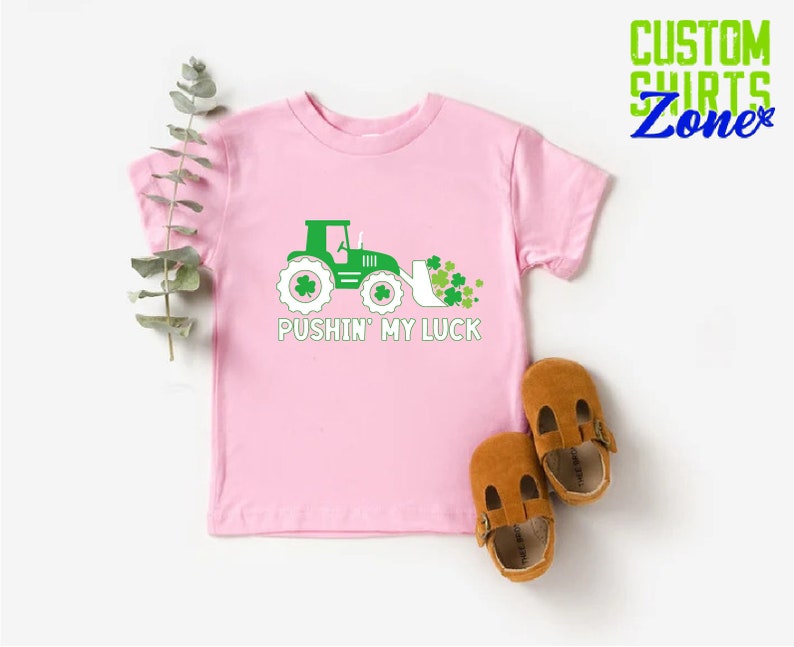 May include: Pink t-shirt with a green tractor and shamrocks, and the text "Pushin' My Luck".