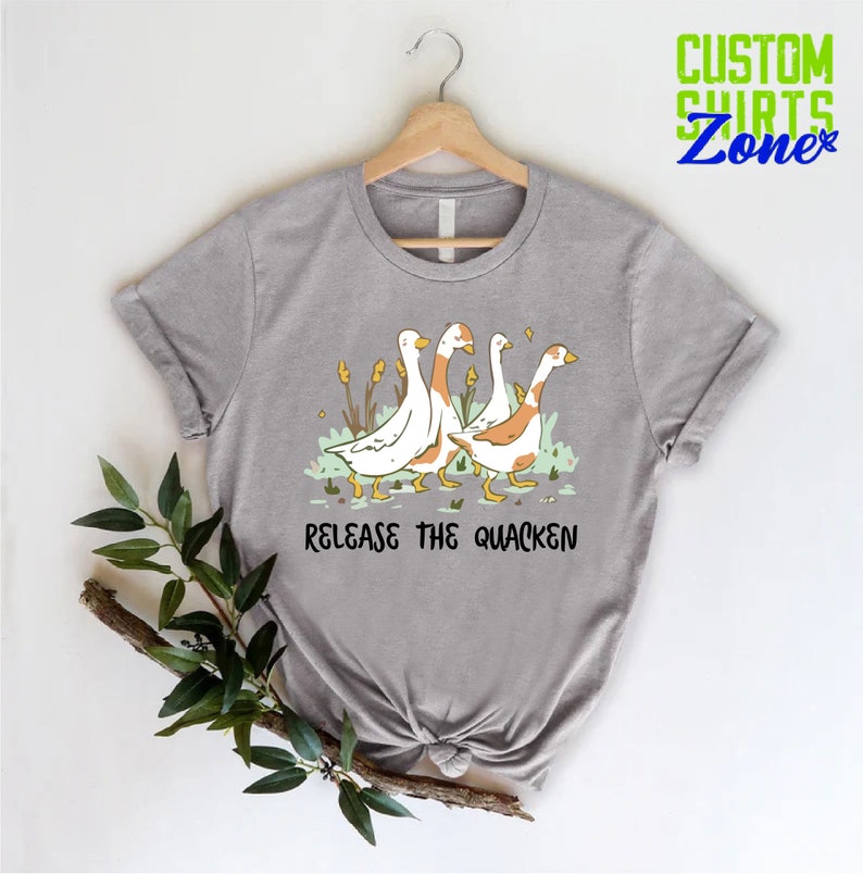 May include: A gray t-shirt with a graphic of four ducks walking in a line. The ducks are white with orange heads and feet. The text "Release the Quacken" is printed below the ducks.