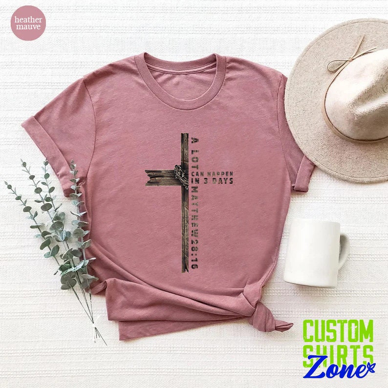 May include: A heather mauve t-shirt with a graphic of a wooden cross and the text "A lot can happen in 3 days Matthew 26:16".