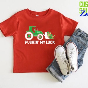 May include: Red short-sleeved t-shirt with a green tractor and shamrocks, and the text "Pushin' My Luck".