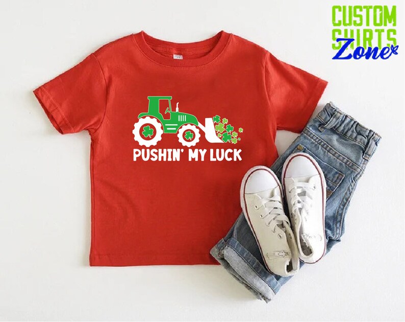May include: Red short-sleeved t-shirt with a green tractor and shamrocks, and the text "Pushin' My Luck".