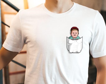 May include: White t-shirt with a pocket featuring a cartoon illustration of a person with a red hat peeking out of the pocket.