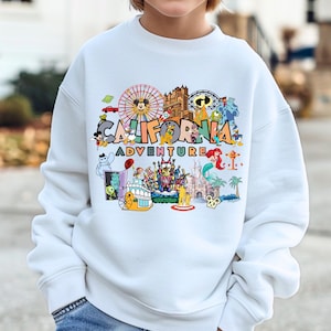 May include: White sweatshirt with a colorful graphic that says "CALIFORNIA ADVENTURE". The graphic includes cartoon images of a Ferris wheel, Mickey Mouse, a castle, and other amusement park elements. The sweatshirt is worn by a person.