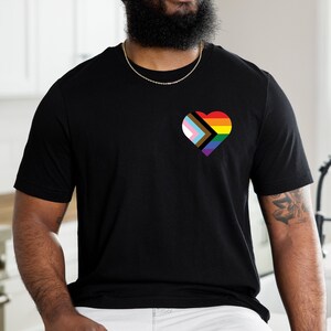 May include: A black t-shirt with a heart-shaped design featuring a rainbow flag with black, brown, pink, blue, and white stripes.