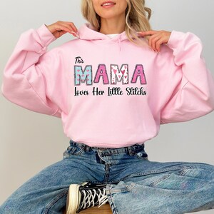 May include: Pink hooded sweatshirt with the text "This Mama Loves Her Little Stitches" in a colorful patchwork font with hearts.