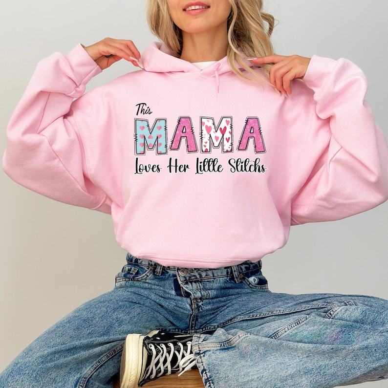 May include: Pink hooded sweatshirt with the text "This Mama Loves Her Little Stitches" in a colorful patchwork font with hearts.