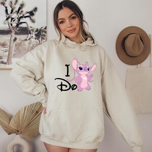 May include: A cream-colored hoodie with a pink Stitch character and the text "I Do" in black.