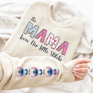May include: A beige sweatshirt with the text "This Mama Loves Her Little Stitches" in pink and blue letters with hearts. The sleeve has three blue Stitch characters with hearts and the names "Robin", "Mary", and "Angel" underneath.