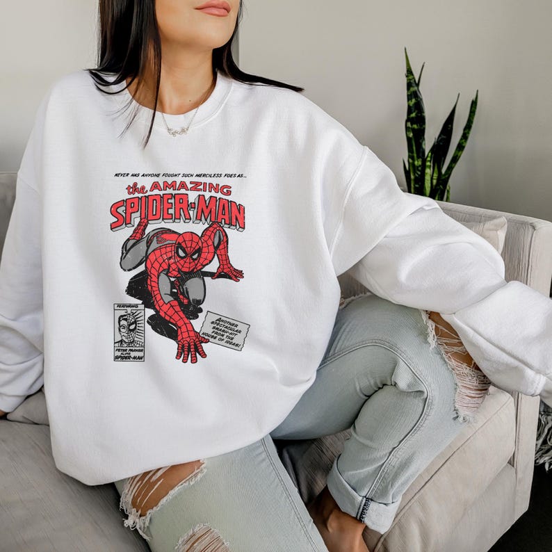 May include: White sweatshirt with a red and blue graphic of Spider-Man. The graphic includes the text "the AMAZING SPIDER-MAN".