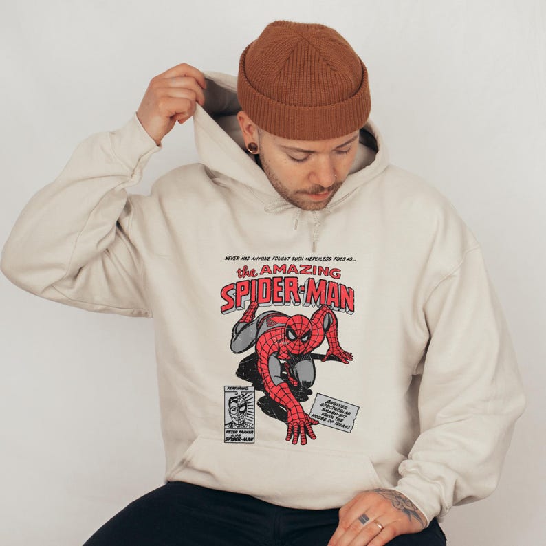 May include: A beige hoodie with a vintage comic book style graphic of Spider-Man. The text on the graphic reads "Never has anyone fought such merciless foes as... The Amazing Spider-Man".
