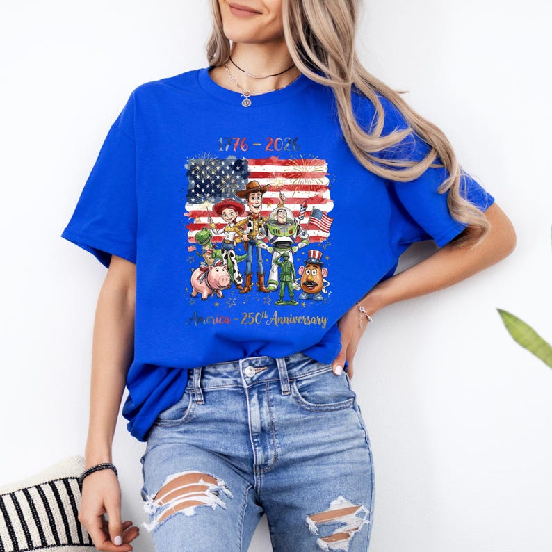 Op de afbeelding: Koningsblauw T-shirt met een afbeelding van tekenfilmfiguren voor een Amerikaanse vlag. De tekst "1776-2026" en "America - 250th Anniversary" staan op het shirt. Het shirt is gemaakt van een zacht materiaal.
