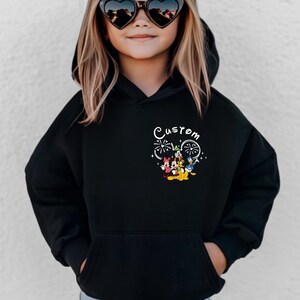K&ouml;nnte beinhalten: Schwarzer Kapuzenpullover mit einem individuellen Design, das Mickey Mouse, Minnie Mouse, Donald Duck, Goofy und Pluto zeigt. Das Design enth&auml;lt Feuerwerk und das Wort "Custom".
