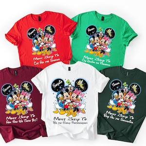 May include: Five brightly coloured t-shirts with a Disney character design. Each shirt is a different colour: red, green, white, burgundy, and dark green. The design includes Mickey Mouse, Donald Duck, Goofy, and other characters. Text on each shirt varies.