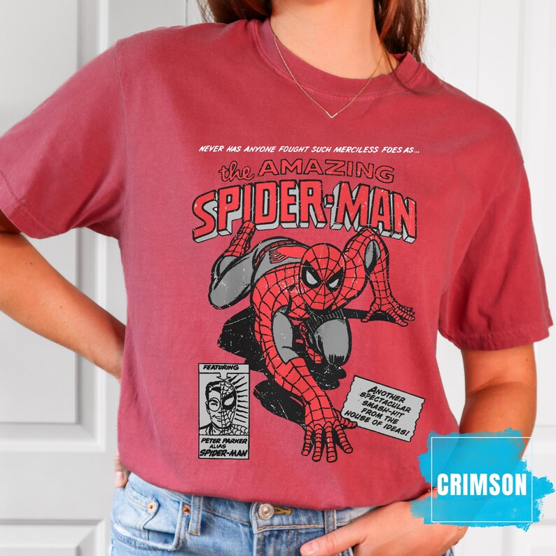 May include: Crimson-colored t-shirt featuring a comic book graphic of Spider-Man in red and gray. The shirt includes text that reads "The Amazing Spider-Man" and other comic book elements. The shirt is a crew neck style.