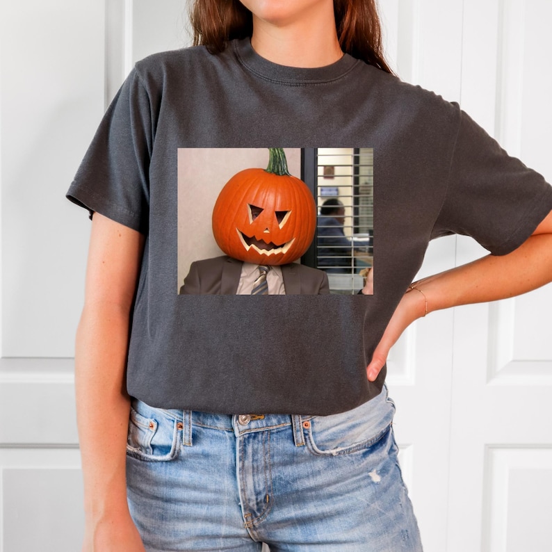 May include: A dark gray t-shirt with a graphic of a person wearing a jack-o'-lantern on their head. The graphic is from the TV show "The Office".