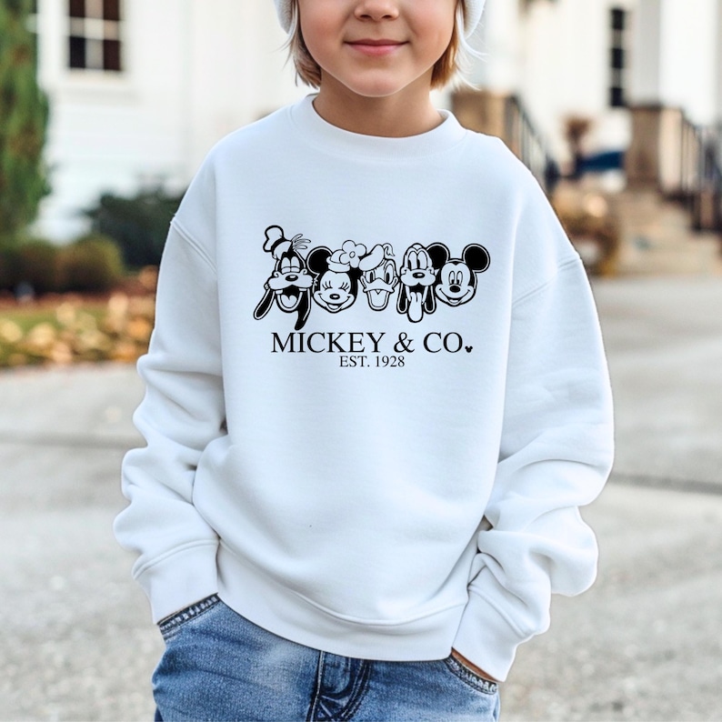 May include: White sweatshirt with a black and white graphic of Mickey Mouse and friends. The text "Mickey & Co. Est. 1928" is printed below the graphic.