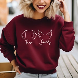 May include: Burgundy sweatshirt with a white outline of two dog heads and the names "Rose" and "Buddy" written underneath.