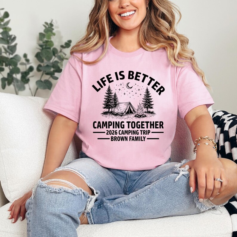 Puede incluir: Camiseta rosa claro con la frase "LIFE IS BETTER" sobre una escena de acampada con una tienda de campa&ntilde;a, &aacute;rboles y una fogata. Debajo, se lee "CAMPING TOGETHER - 2026 CAMPING TRIP - BROWN FAMILY".
