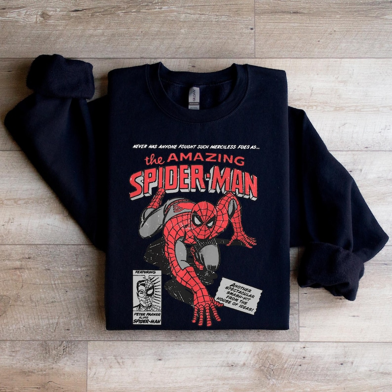 May include: Black sweatshirt with a vintage comic book design featuring Spider-Man. The text reads "NEVER HAS ANYONE FOUGHT SUCH MERCILESS FOES AS... the AMAZING SPIDER-MAN".