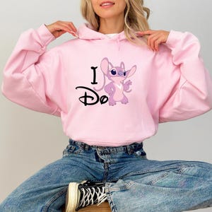 May include: Pink hooded sweatshirt with a cartoon Stitch character and the text "I Do" printed on the front.