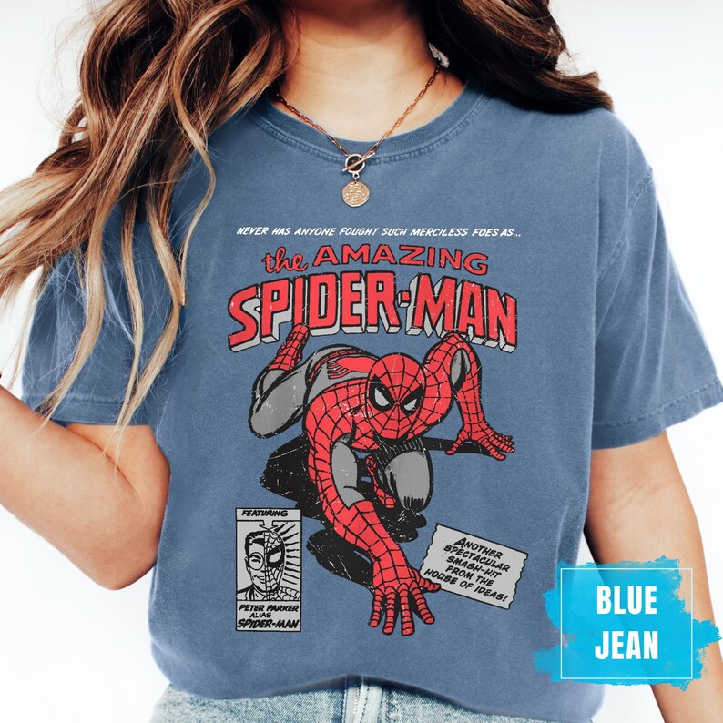 May include: Blue jean t-shirt featuring a vintage comic book graphic of Spider-Man. The design includes the text "the AMAZING SPIDER-MAN" in red and white, along with comic book panels and text. The shirt is a solid blue color.