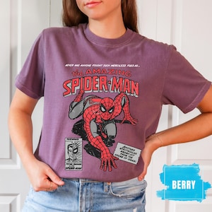 May include: Berry-colored t-shirt featuring a comic book graphic of Spider-Man. The design includes the text "the AMAZING SPIDER-MAN" in red and white, with additional text and a comic panel illustration.