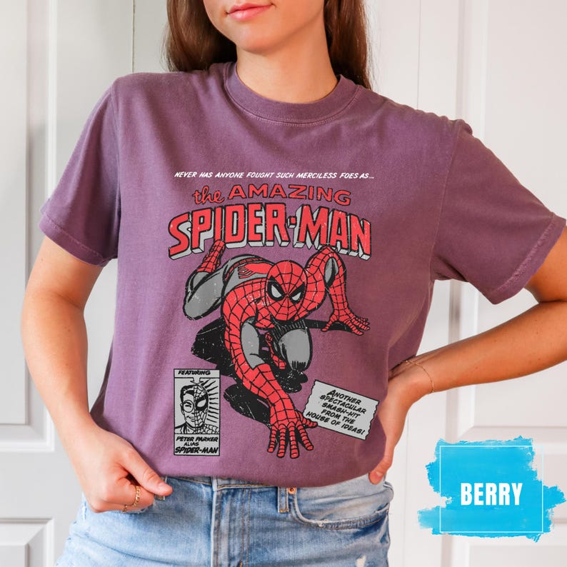 May include: Berry-colored t-shirt featuring a comic book graphic of Spider-Man. The design includes the text "the AMAZING SPIDER-MAN" in red and white, with additional text and a comic panel illustration.