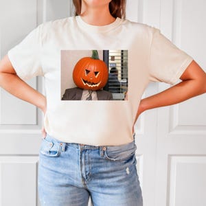 May include: A white t-shirt with a graphic of a person with a pumpkin head. The pumpkin has a carved jack-o'-lantern face. The person is wearing a suit and tie. The graphic is from the TV show "The Office".