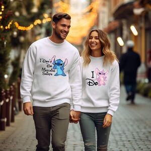 May include: A couple wearing white sweatshirts with a blue and pink Stitch character graphic. The man's shirt says "I Don't Do Matching Shirts" and the woman's shirt says "I Do".