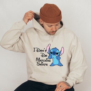 May include: A beige hoodie with a blue Stitch character from Lilo & Stitch. The hoodie has the text "I Don't Do Matching Shirts" printed on it.