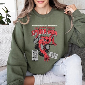 May include: Green sweatshirt with a vintage comic book design featuring Spider-Man. The text reads "Never has anyone fought such merciless foes as... the Amazing Spider-Man".