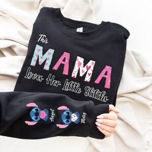 May include: Black sweatshirt with the text "This Mama Loves Her Little Stitches" in pink and blue letters with hearts. The sleeves have blue Stitch characters with pink hearts and the names "Angel" and "Mary" written in pink.
